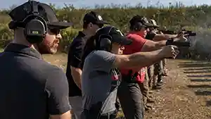 A line of shooters on a shooting range firing their semi-automatic pistols.