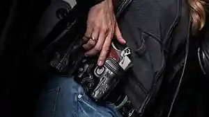Woman with hand on an OWB holstered semi–automatic pistol.