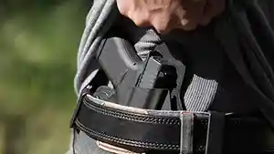Man showing IWB holstered semi–automatic pistol under shirt.