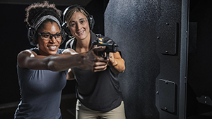 Woman showing another woman how to shoot a pistol at an indoor shooting range.