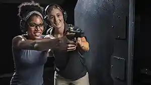 Woman showing another woman how to shoot a pistol at an indoor shooting range.