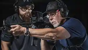Man showing another man how to shoot a rifle at an indoor shooting range.