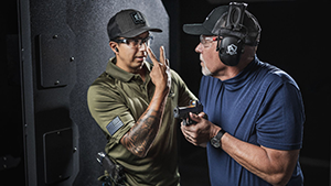 Man trying to get the attention of another man holding a semi–automatic pistol at an indoor shooting range.
