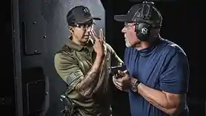 Man trying to get the attention of another man holding a semi–automatic pistol at an indoor shooting range.